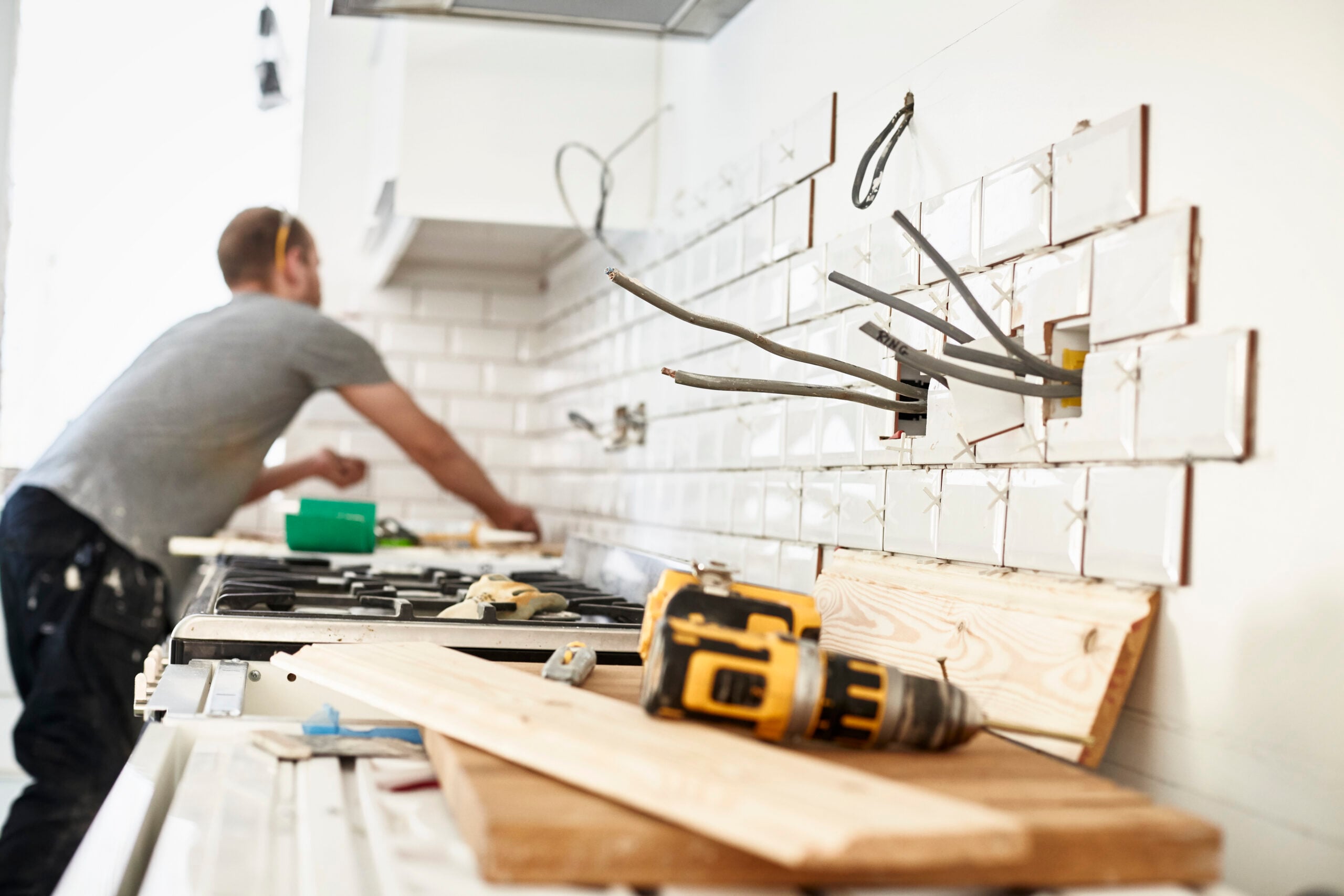 London,England,A man working in a new kitchen, a tiler applying tiles to the wall behind the cooker.