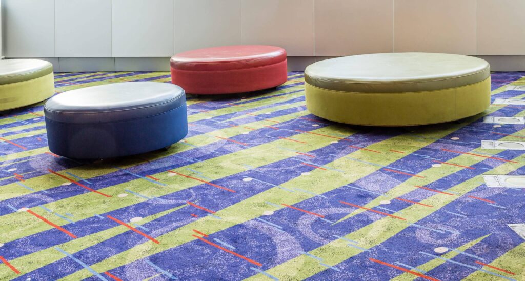 Colorful round and oval upholstered ottomans arranged over vibrant blue and green patterned carpet flooring in Ocala, FL.