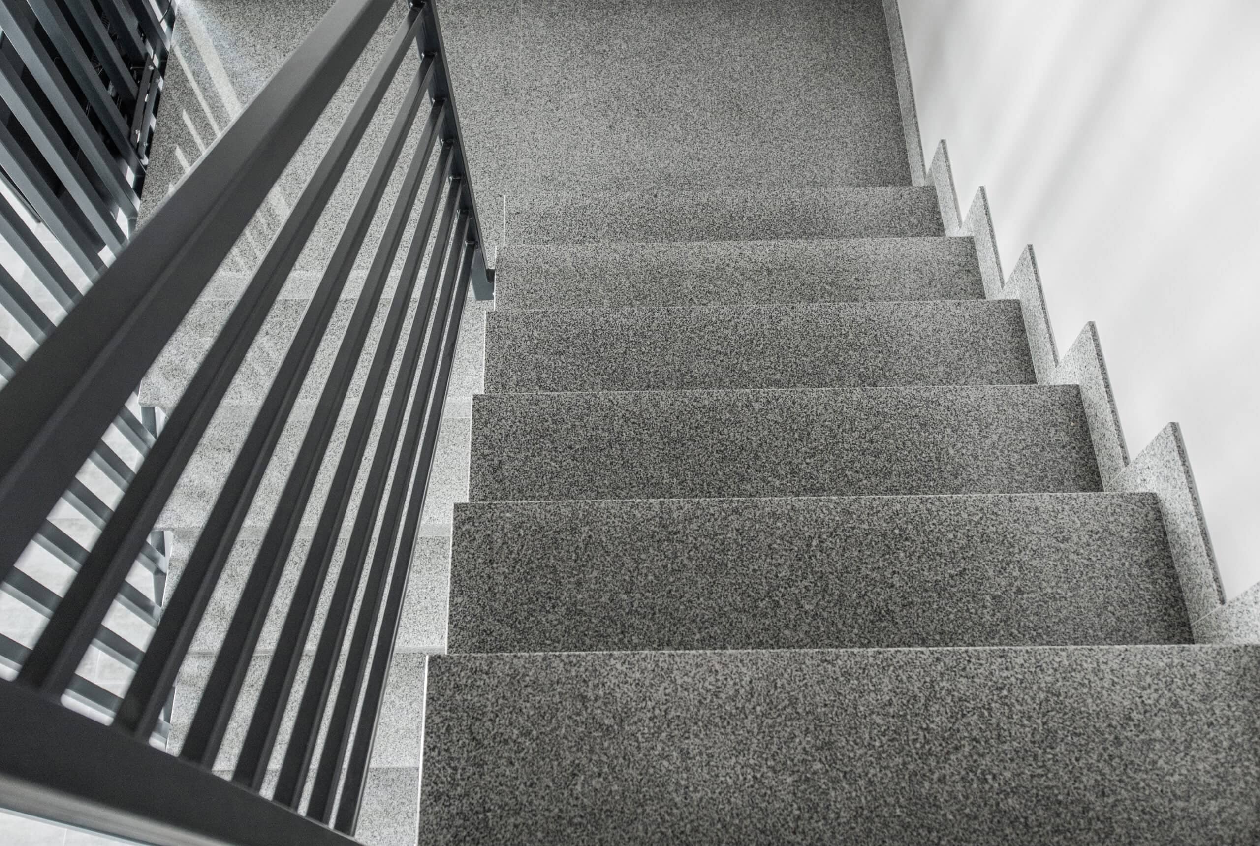 High-angle view of a professionally carpeted staircase featuring durable gray commercial carpeting and modern black metal handrails in Citrus County, FL.