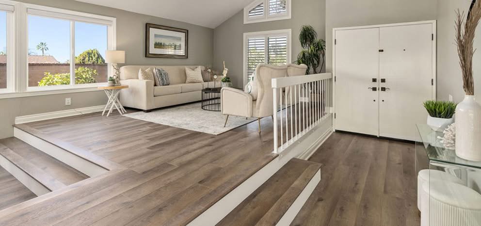 Services 1 Sunlit sunken living room and entry foyer with dark oak LVP flooring installation, custom white baseboard trim, steps, and interior double doors in The Villages, FL.